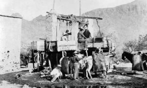 Miners operate a hydraulic sluice in San Francisquito Canyon, Los Angeles County. The placer mine machine consists of adobe columns, pulleys, ropes, and wood boxes. Donkeys are loaded with ore bags.