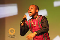 Man wearing red shirt and gold chain performing with microphone in hand