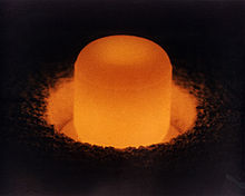 Glowing cylinder of plutonium oxide standing in a circular pit