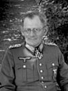 A man wearing a military uniform and glasses with an Iron Cross displayed at the front of his uniform collar.