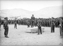 A military officer on a podium delivers a speech to gathered troops
