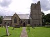 Stone church with square tower. In the foreground are a path and gravestones