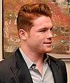 A man in his early twenties sporting ginger hair and goatee with a smile