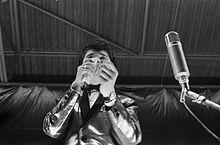 A black and white photo of singer Vince Taylor in front of a microphone