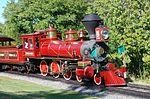 A red steam locomotive with a 4-6-0 wheel arrangement (four leading wheels, six driving wheels, and no trailing wheels) and its tender