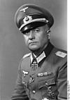 A man wearing a military uniform, peaked cap and neck order in the shape of a cross.