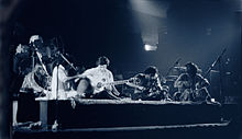 A quartet performs acoustic music to the audience while being covered by a dark stage-light.