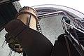 On the left of the picture is a large medium brown cylinder oriented vertically; this is the telescope tube. The dark brown fork of the equatorial mount is in the foreground, connecting from its base at the bottom right to the side of the telescope tube. On the right, a person has reached the top of a staircase. At the top of the picture, an overexposed sky (appearing white) can be seen through the open observing slit.