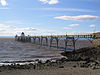 Metal pier standing on thin legs rising from the sea. Beach in the foreground