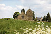 Stone building with tower beyond field and stone wall.