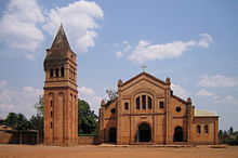 Photograph depicting the Roman Catholic parish church in Rwamagana, Eastern Province, including the main entrance, fa&ccedil;ade, the separate bell tower, and dirt forecourt